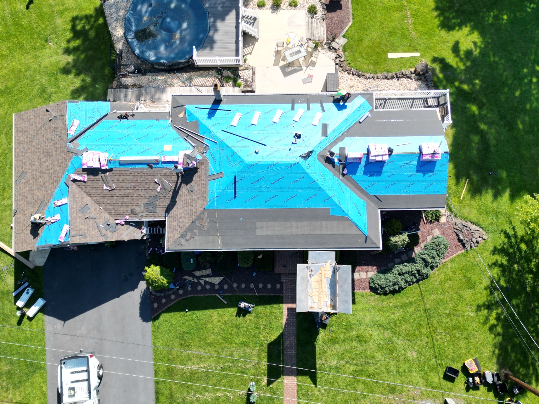 Aerial view of a single-story home during roof replacement with blue tarps and materials staged by REP
