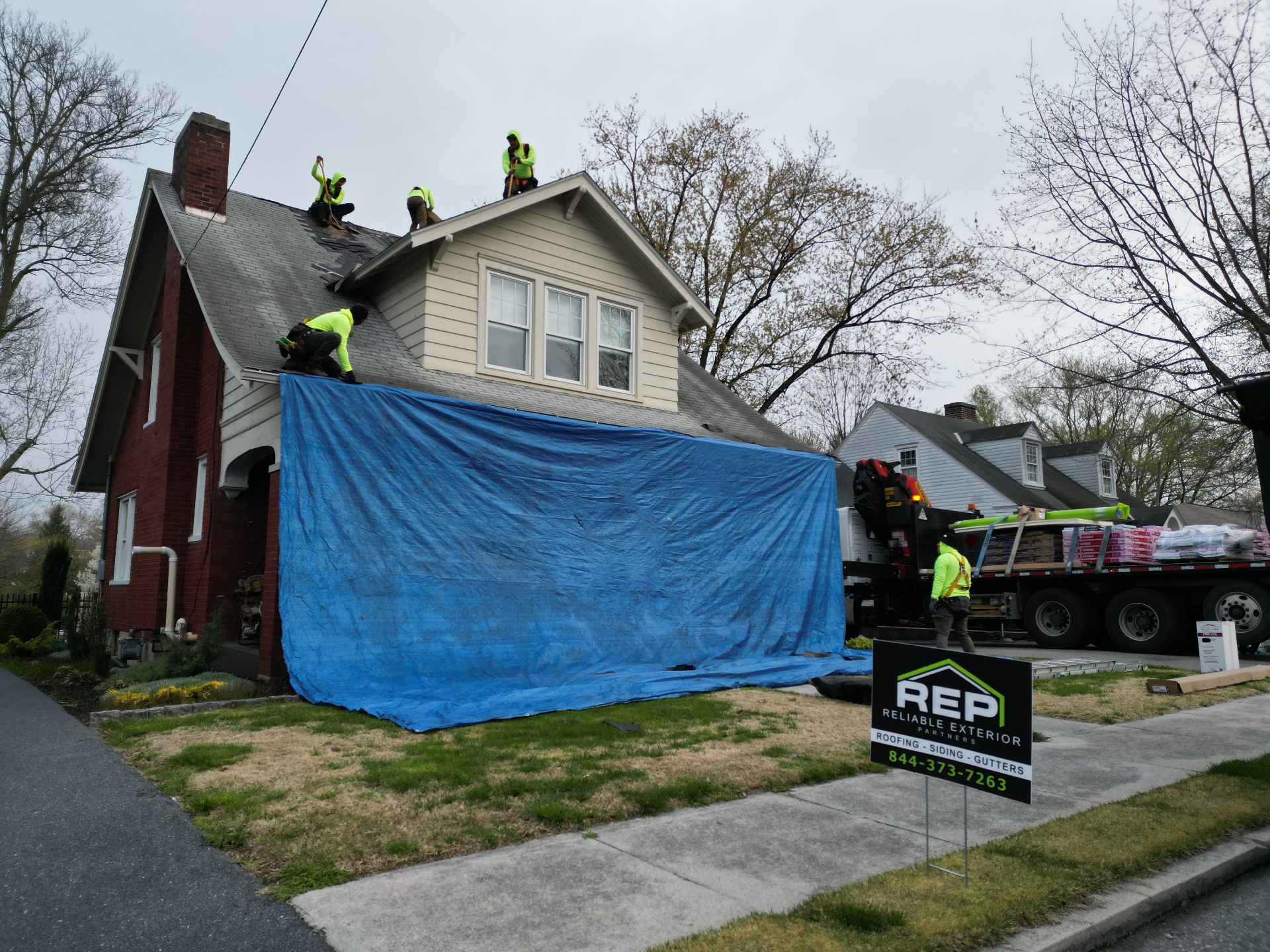 Ground view of a brick home during roof replacement with REP crew and property protection in place