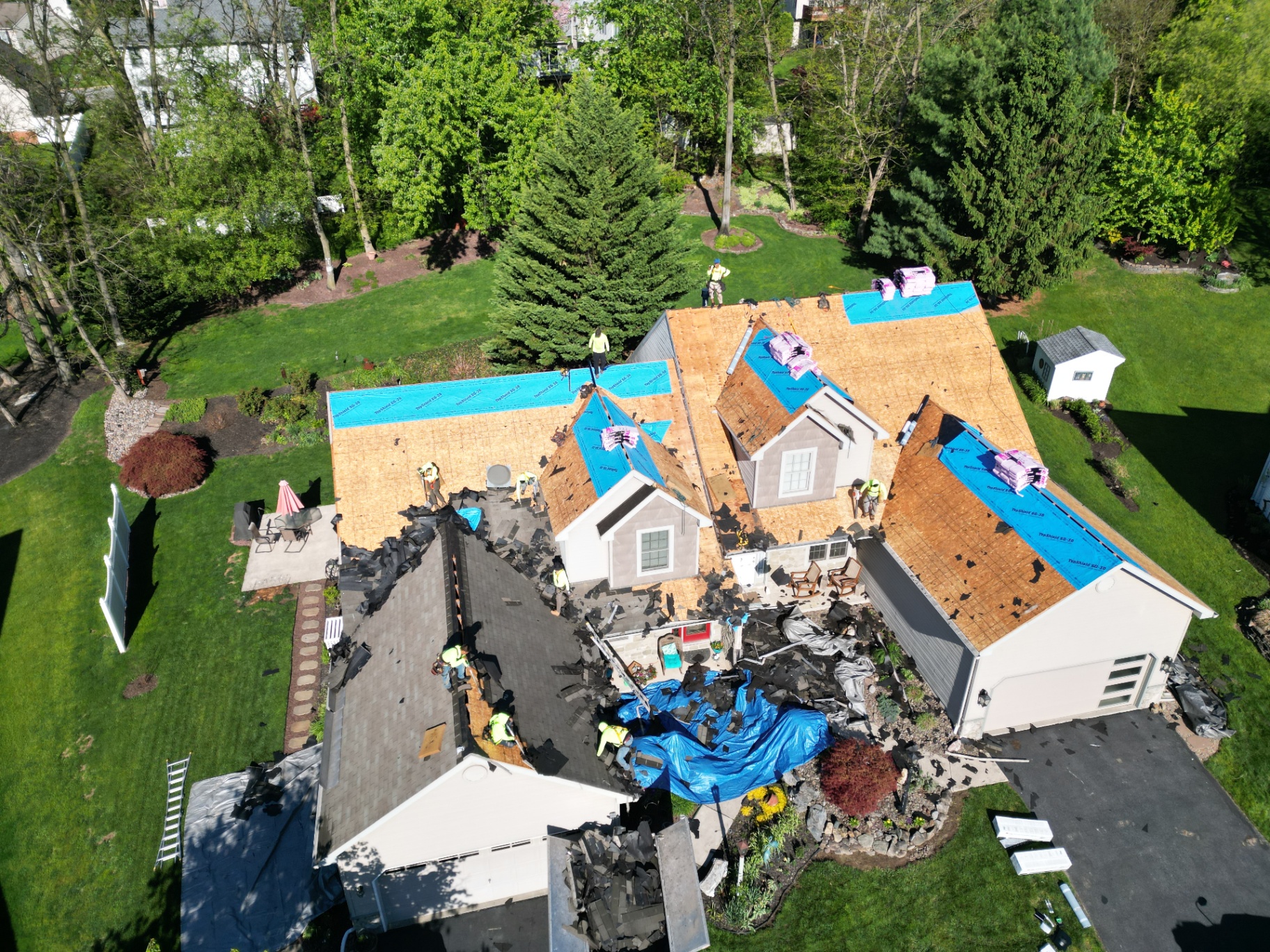 Aerial view of a suburban home during roof replacement with decking exposed and REP crew working